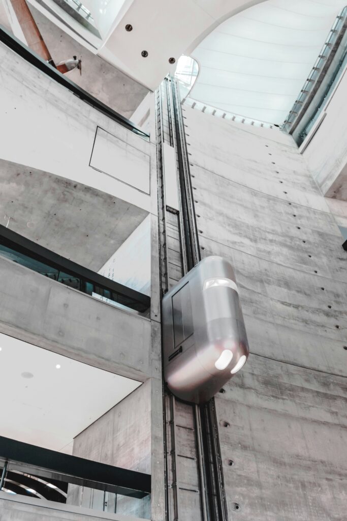 A chrome elevator, rising up a concrete building. 