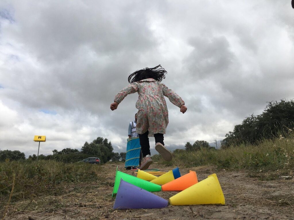 A girl jumps over colorful cones. 