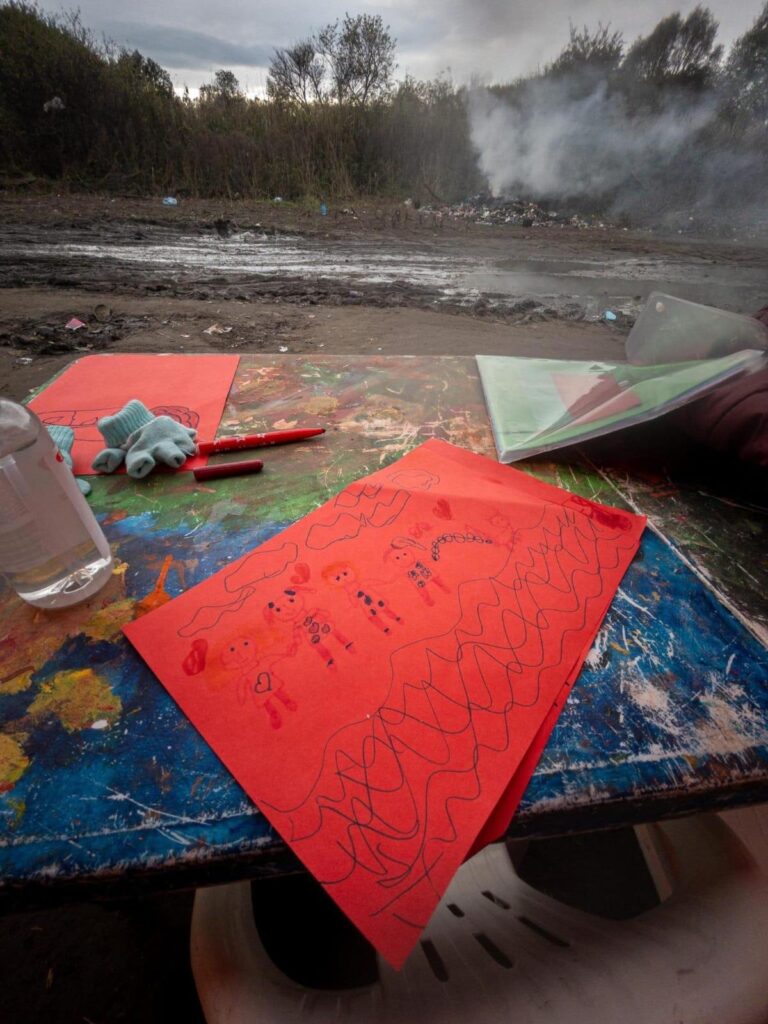Children’s drawings and drawing materials are laid out in a muddy path.