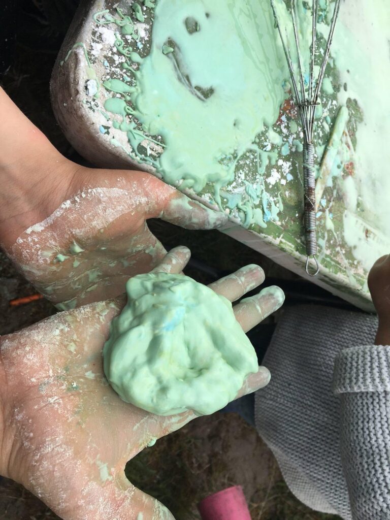 A hand holds some sort of green slime or putty. 