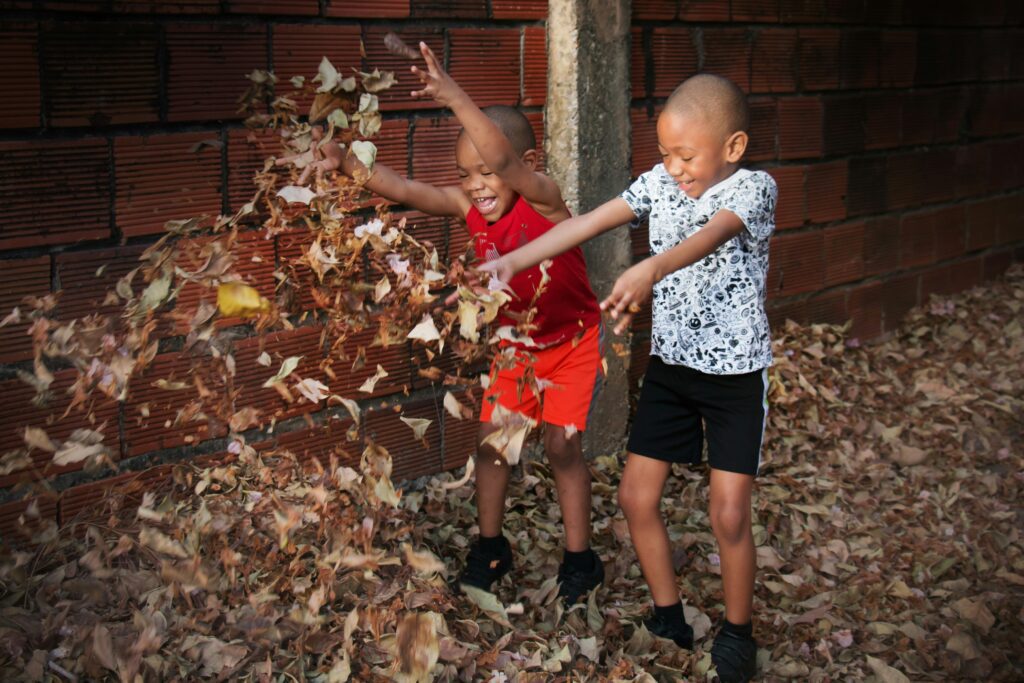 Two boys digging dry leaves near brick wall