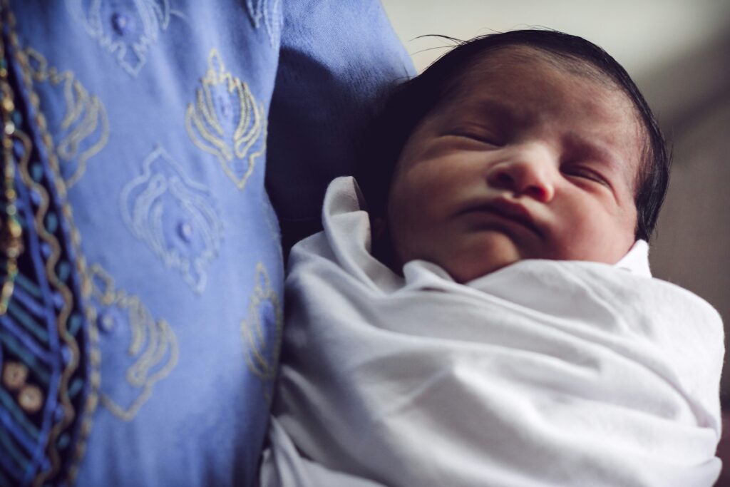 An infant in swaddle sleeps while held in their loved one’s arms.