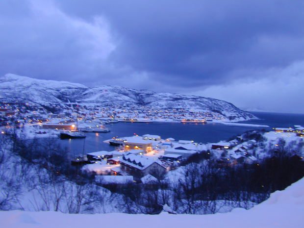 A Norwegian town, built upon a sea channel and surrounded by mountains, is dusted in fresh snow.