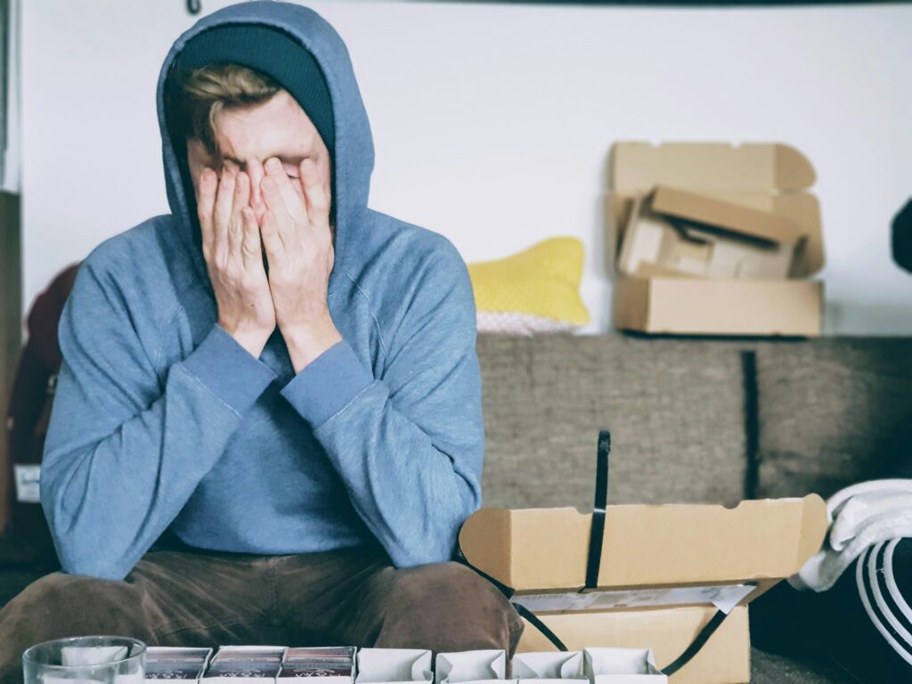 Image of a person holding their head in their hands in a cluttered space.