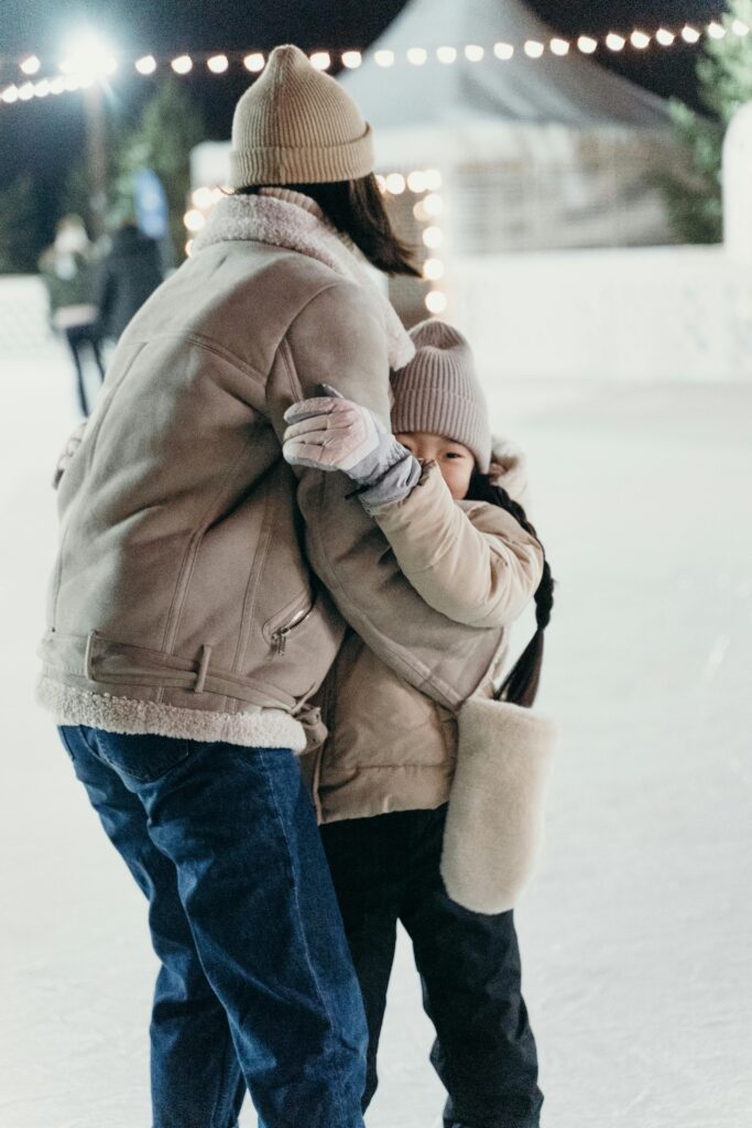 A grandmother hugs her granddaughter lovingly on a cold night. She is a kinship carer, and her granddaughter stares at the camera warmly.