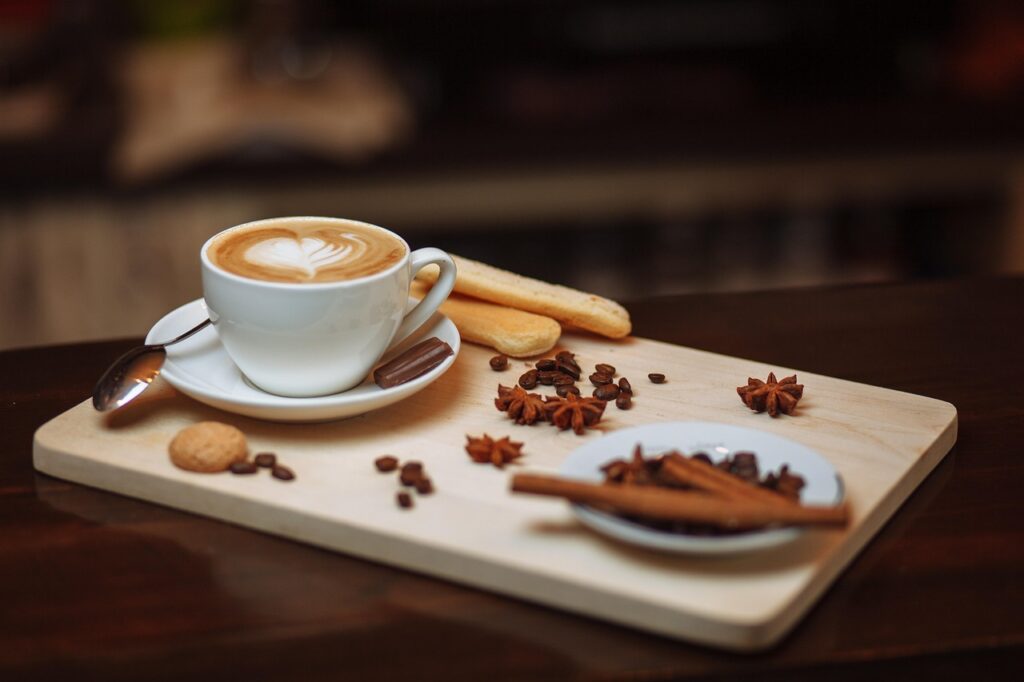 A cup of latte on a wooden tray with scattered pumpkin-pie spices and ladyfinger cookies