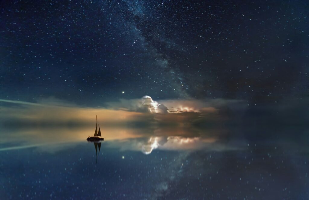 Image of a sailboat floating on the water. Above is a night sky filled with stars.