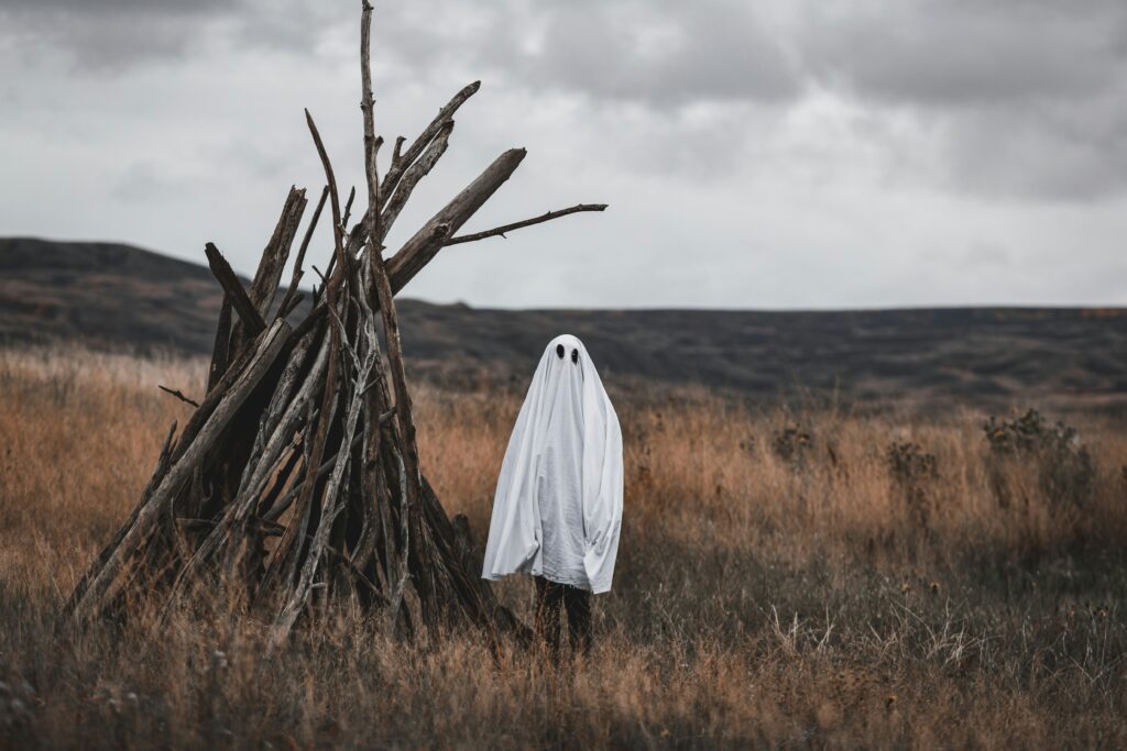Ghostly costume beside unlit pyre in bare field, Saskatchewan, Canada