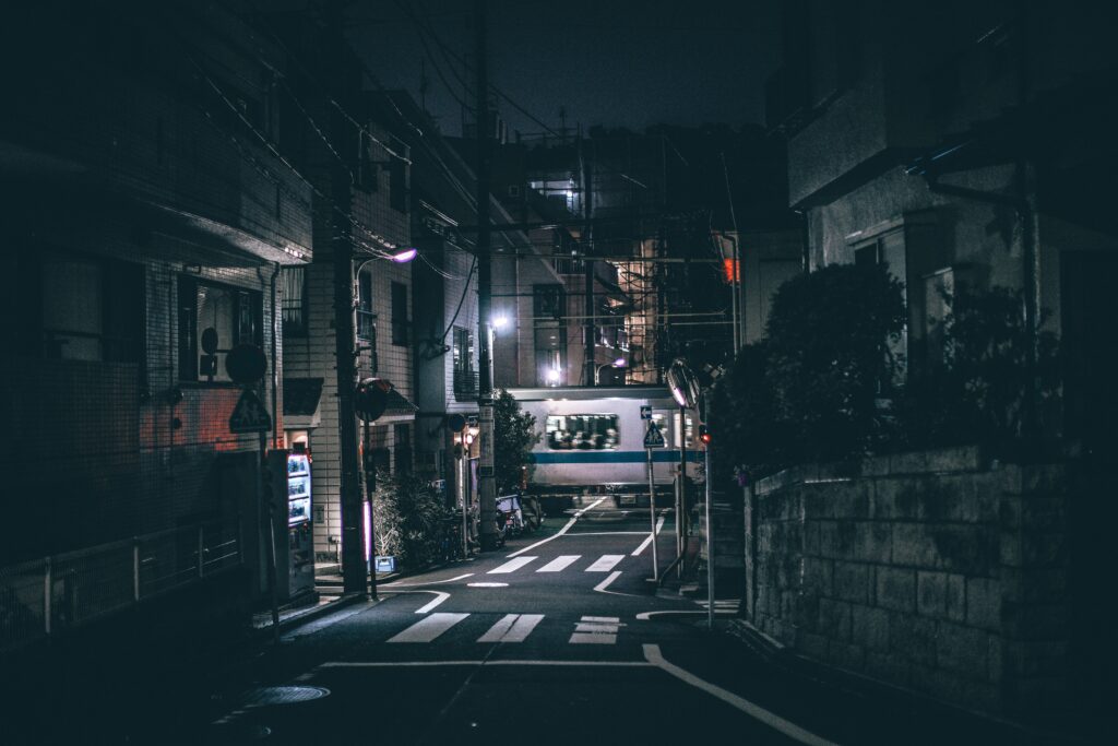  Image of a dark city road at night. In the background, a train flashes by.