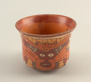 Earth-toned orange-brown-yellow-tan ceramic beaker with a shocked-looking human face framed by a self-satisfied bat with outstretched wings.