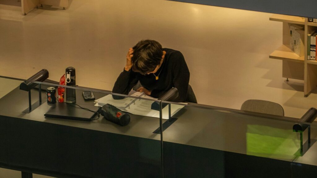 Image of person sitting at a desk, head lowered, looking intently at their work.