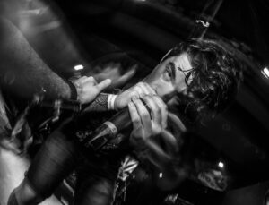 Intense-looking male singer caresses a mic while embraced by a crowd