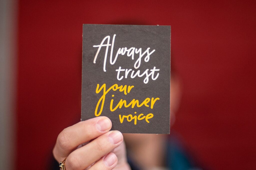Always trust your inner voice, an affirmation, shown on a card held high, masking the face behind it.