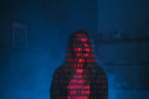A woman sits in the dark while red binary text covers her body and conceals her identity.
