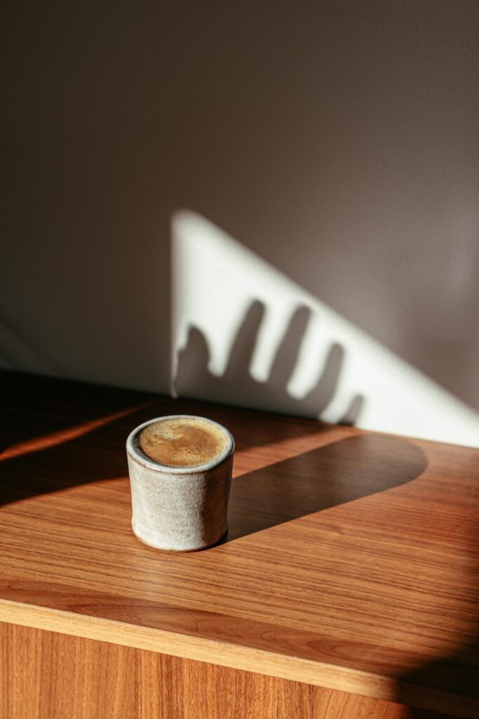 A shadowy hand reaches for a coffee drink on a wooden table.