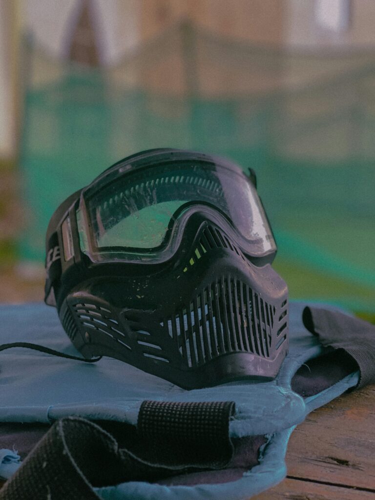 A close up picture of a full-face mask and goggles, resting on a tactical vest.