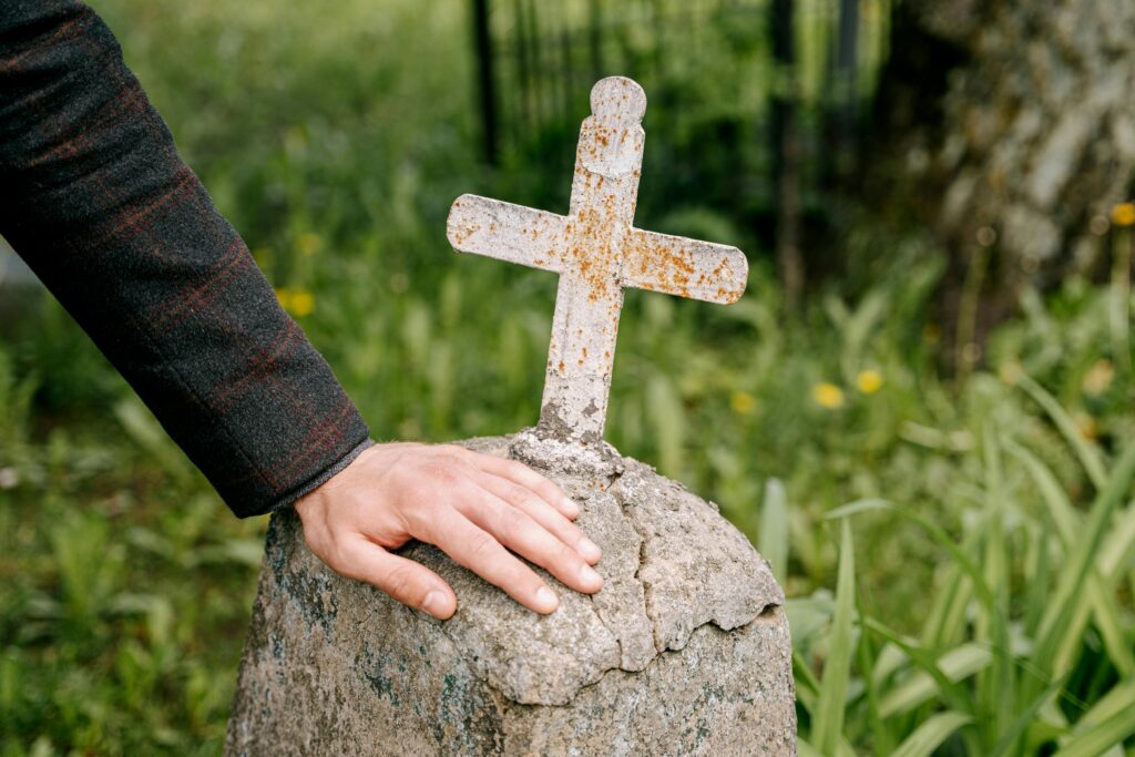 A person touches an old gravestone with a cross.