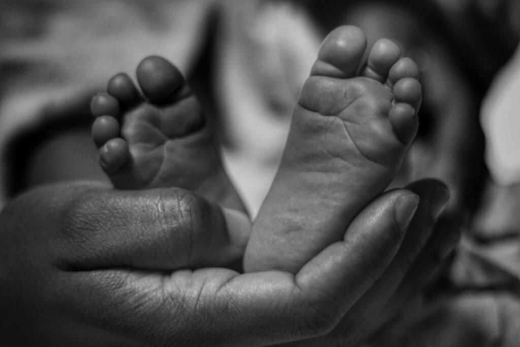 A black and white photograph of an adult hand cradles two baby feet gently, protecting them.