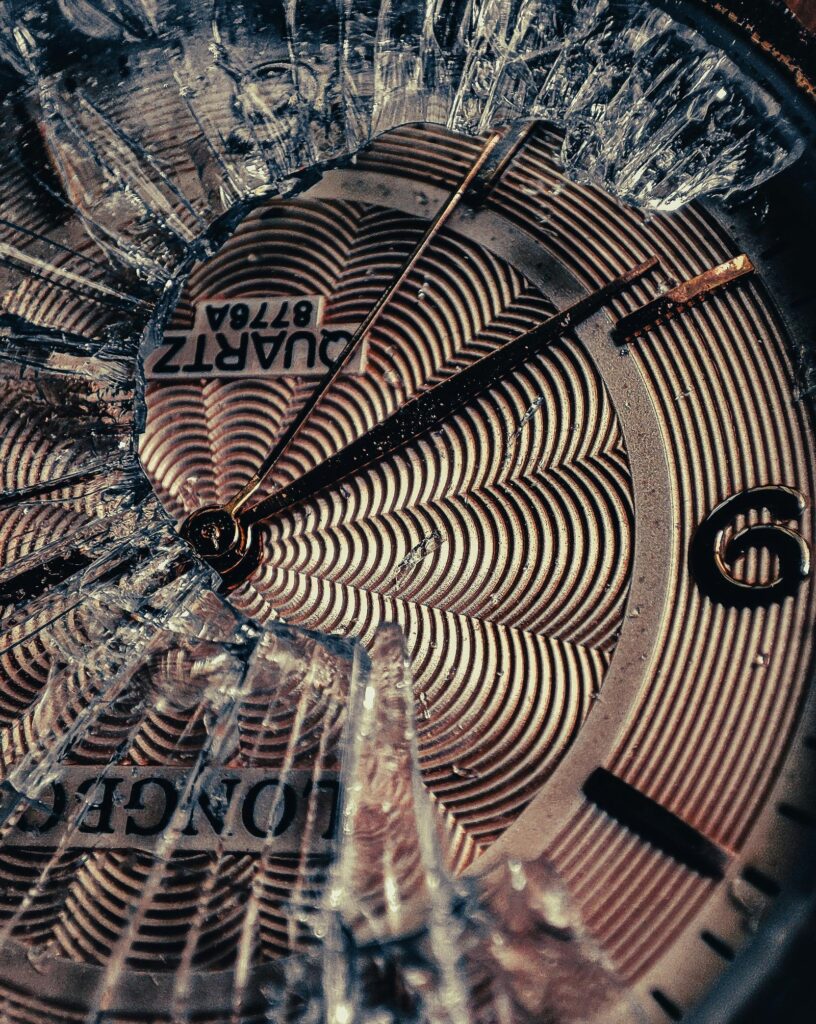 A broken clock, with shattered glass on its face, shines.
