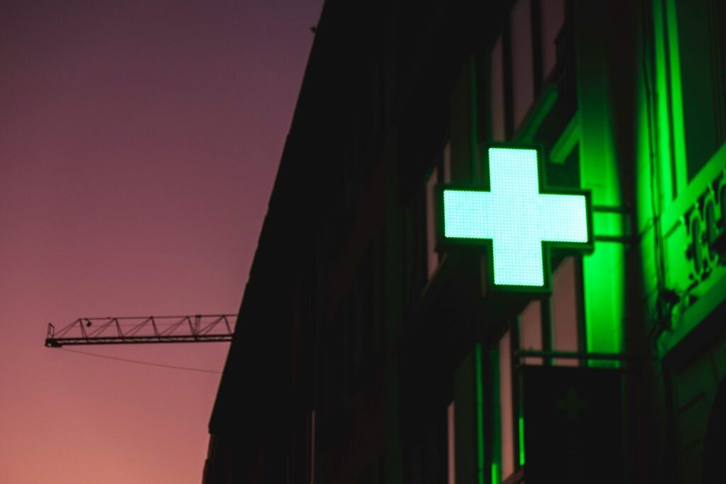 A glowing green sign of a pharmacy against a sunset.