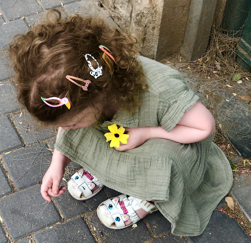 A young girl crouching on the ground, picking up a piece of grass.
