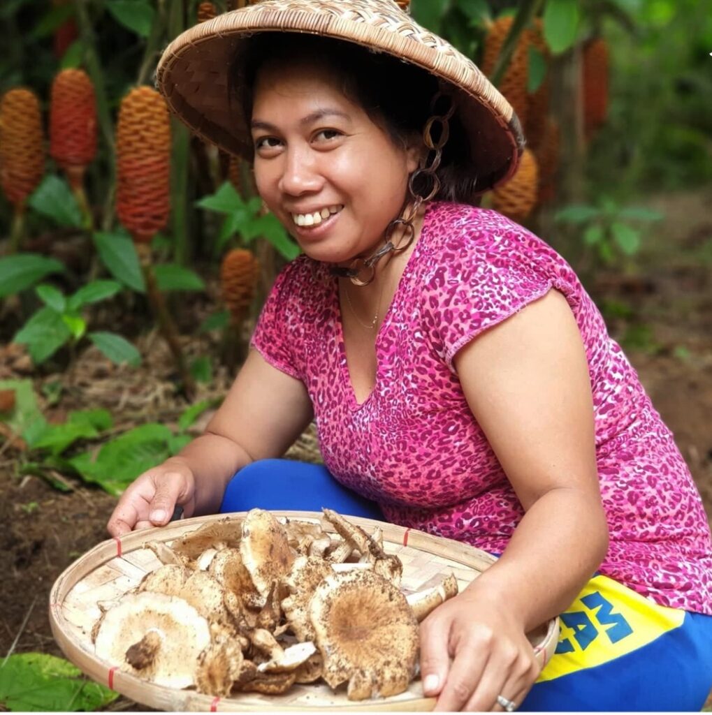 A woman holds a pallet of large mushrooms. 