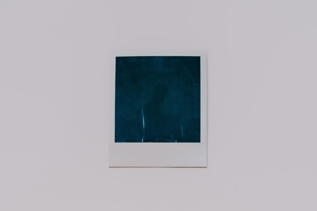 Image of a polaroid picture on a white background. The polaroid picture is dark and difficult to make out what, or who, the subject is.