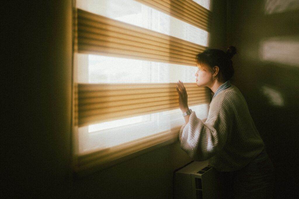 Image of a woman peeking out a window through window blinds.