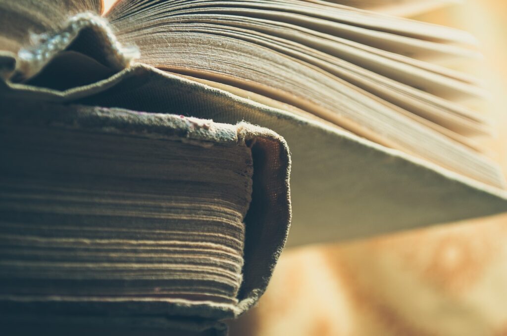 Two weathered books stacked on top of each other. The top book is open in the middle.