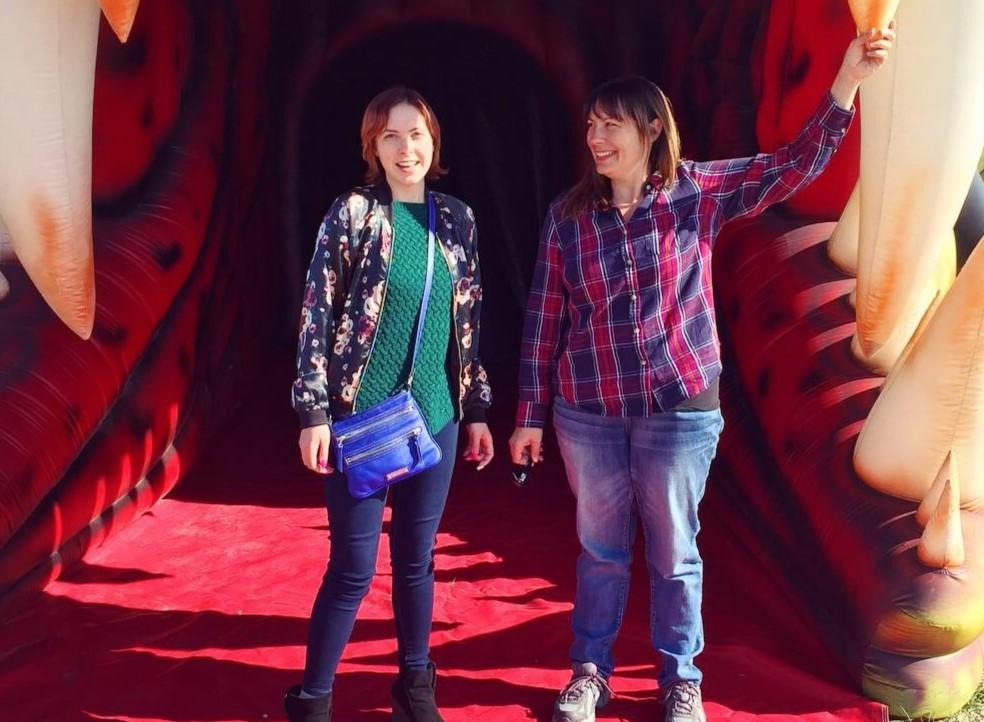 Two people smiling while standing in the reproduction of a dinosaur.