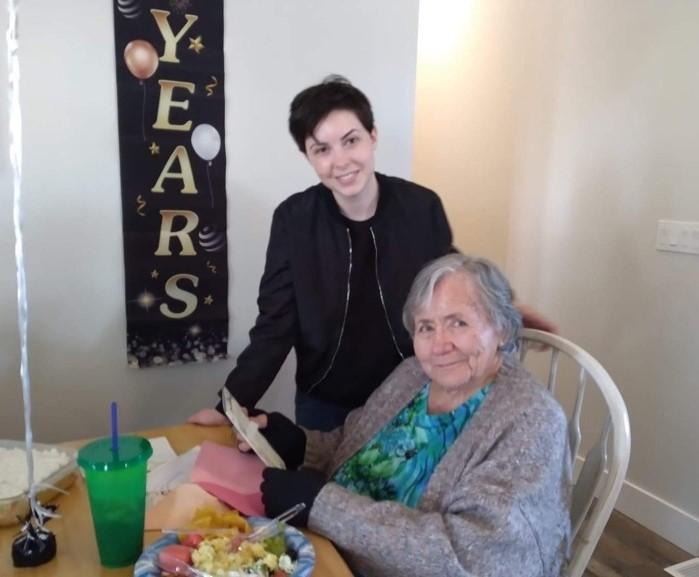 Brooklyn Riepma with their grandmother, the latter sitting at a table.