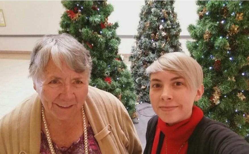 A photo of Brooklyn Riepma with their grandmother in front of three Christmas trees on display. 