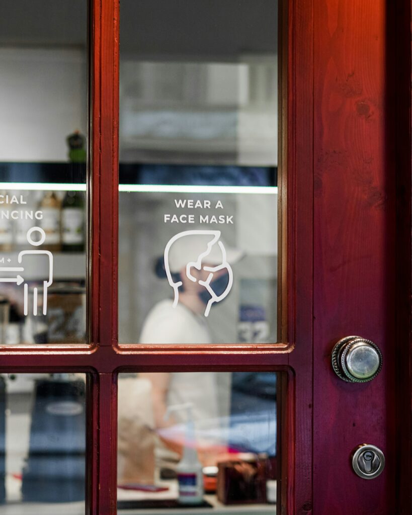 The door to a business that has a decal in the window, asking patrons to wear a face mask.