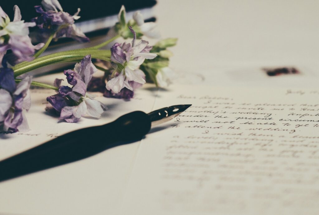 Image of a handwritten letter. There are a bundle of small, purple flowers and an inkwell pen on the letter.