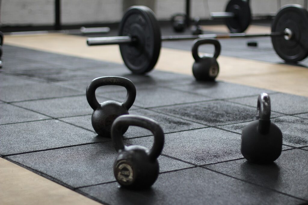 A series of kettlebells and a weighted barbell on a matted gym floor.