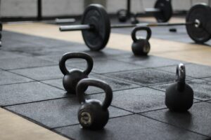 A series of kettlebells and a weighted barbell on a matted gym floor.