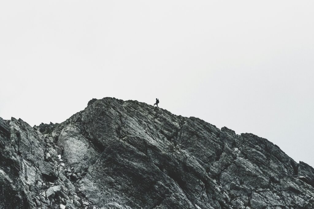 Greyscale photo of a person trekking across a rocky mountain