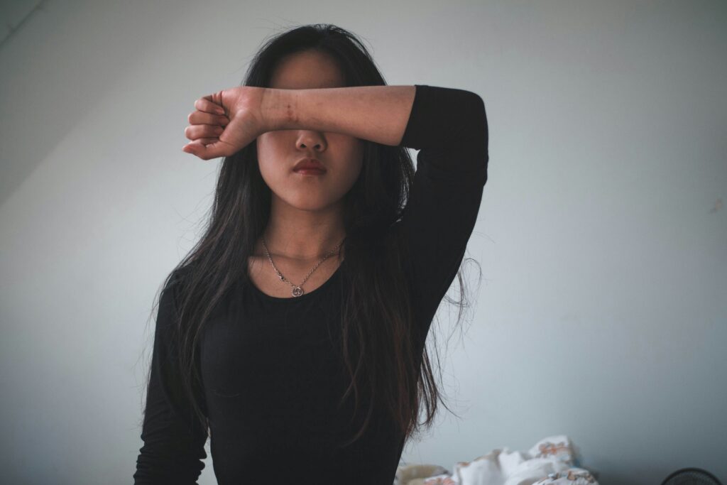 A young woman standing, with her forearm crossed over her eyes.