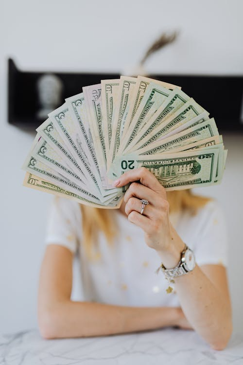 A man holding 5, 10, and 20 dollar bills with his face covered.