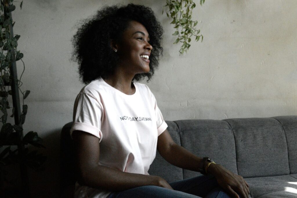 Image of a woman sitting on a couch, smiling at something or someone off camera.