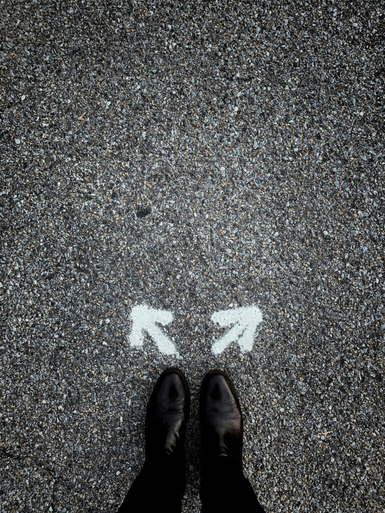 Two feet behind two arrows spray-painted onto asphalt. The arrows are pointing in two different directions.