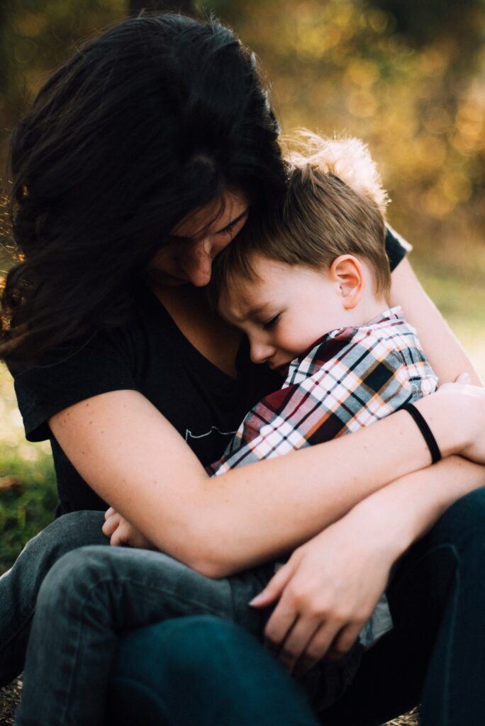 Image of a woman hugging a young boy sitting on her lap. The boy appears upset.