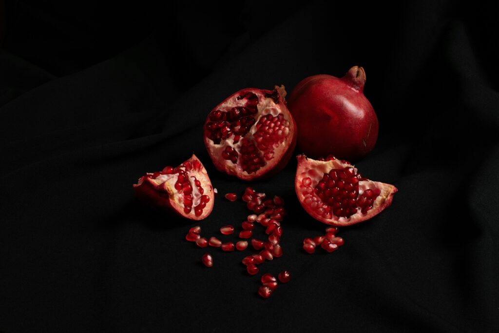 An open pomegranate, seeds spilling from the center, against a black background.