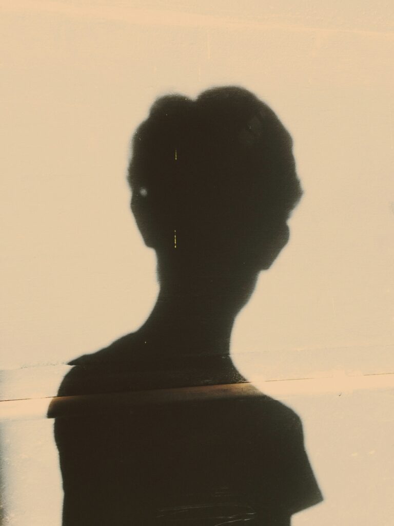 The shadow of the back of a person’s body projected onto a tan wall. 