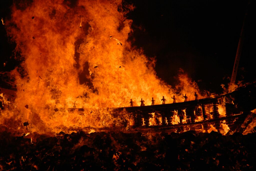 A fire burning, figures darkened in its light.