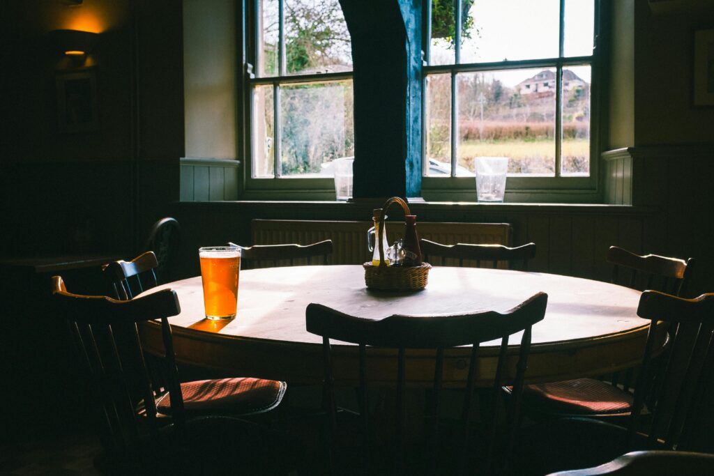 The dark interior of a building, chairs around a table that has one filled pint glass on it. 