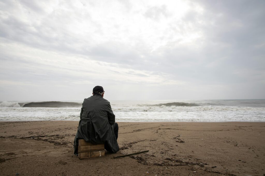 Image of a person sitting on the beach, staring out at the ocean.