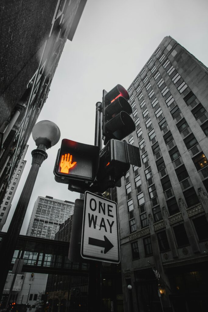 A red hand signal stops pedestrian traffic above a one-way sign.