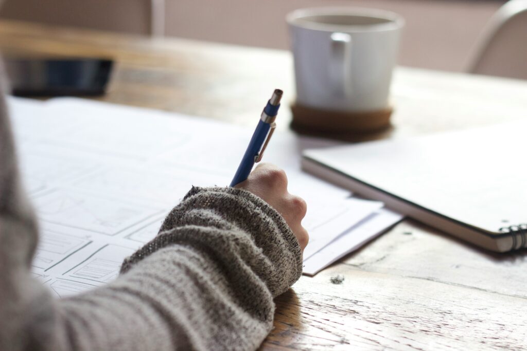A hand, holding a ball point pen, writing on paper.