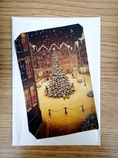  A Christmas card featuring a Christmas tree ornately decorated in a town square. 